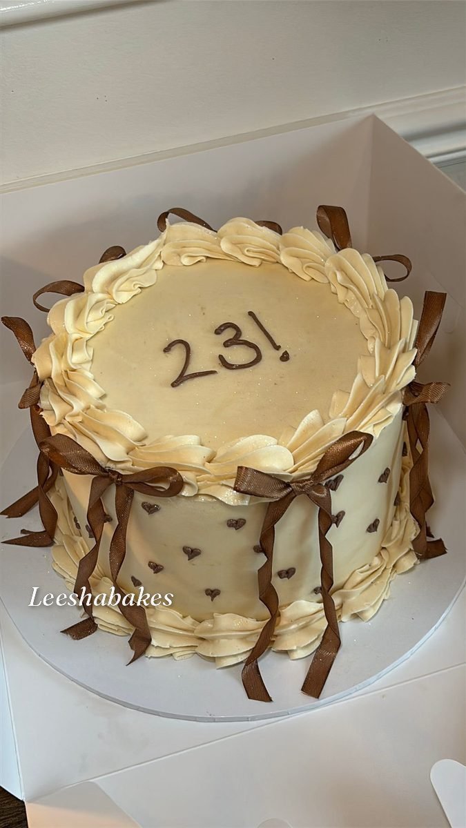 Cream round cake with brown bows, tiny hearts and '23' message
