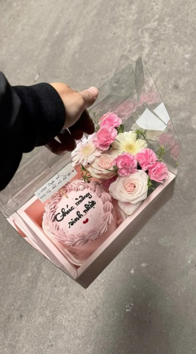 Pink heart cake with a piped border in a clear box with fresh flowers